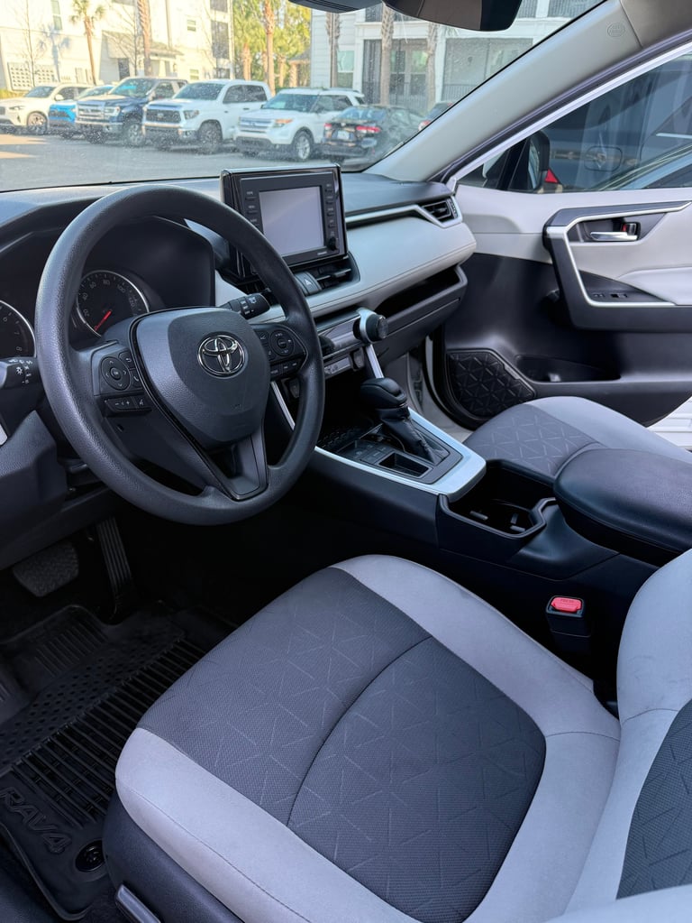 Interior view of a Toyota vehicle showing steering wheel, dashboard with touchscreen, and two-tone black and white seats