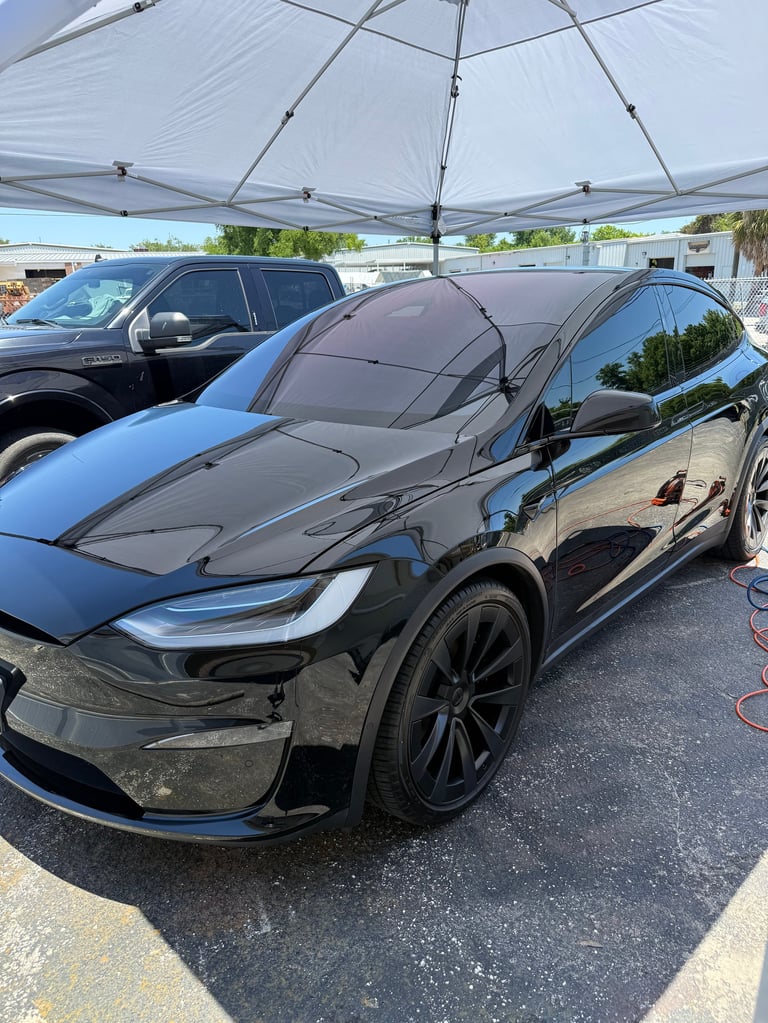Black Tesla electric car parked under a pop-up canopy at an outdoor lot, showing front quarter view