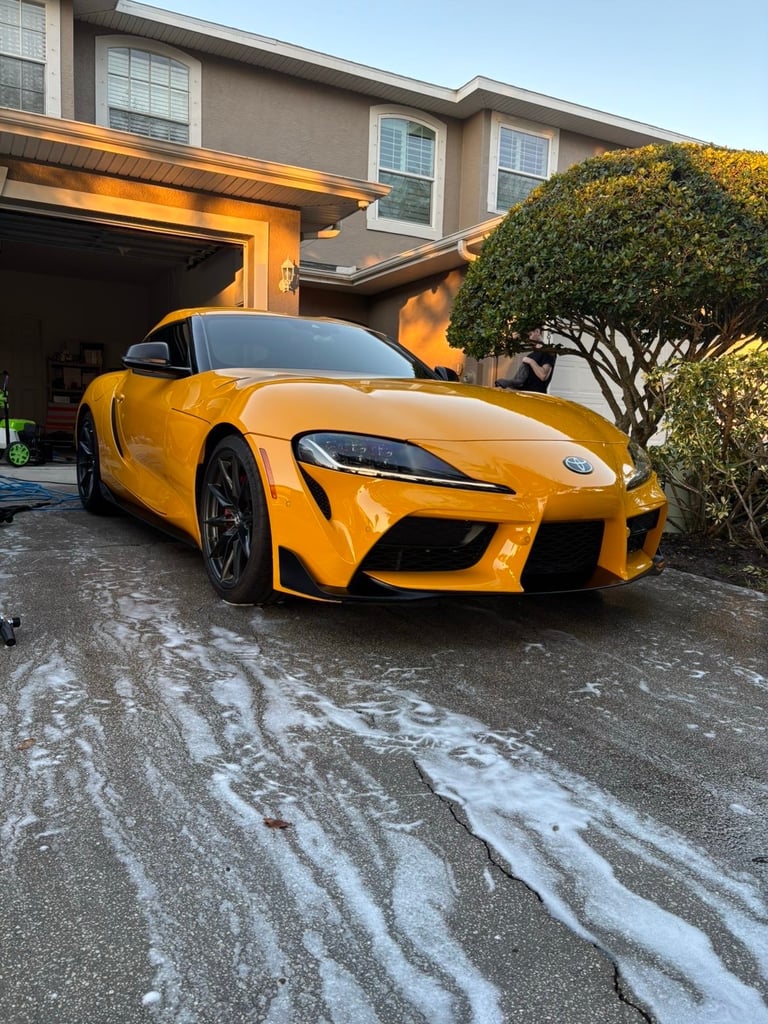 Bright yellow sports car parked in driveway of modern house with garage and green shrub