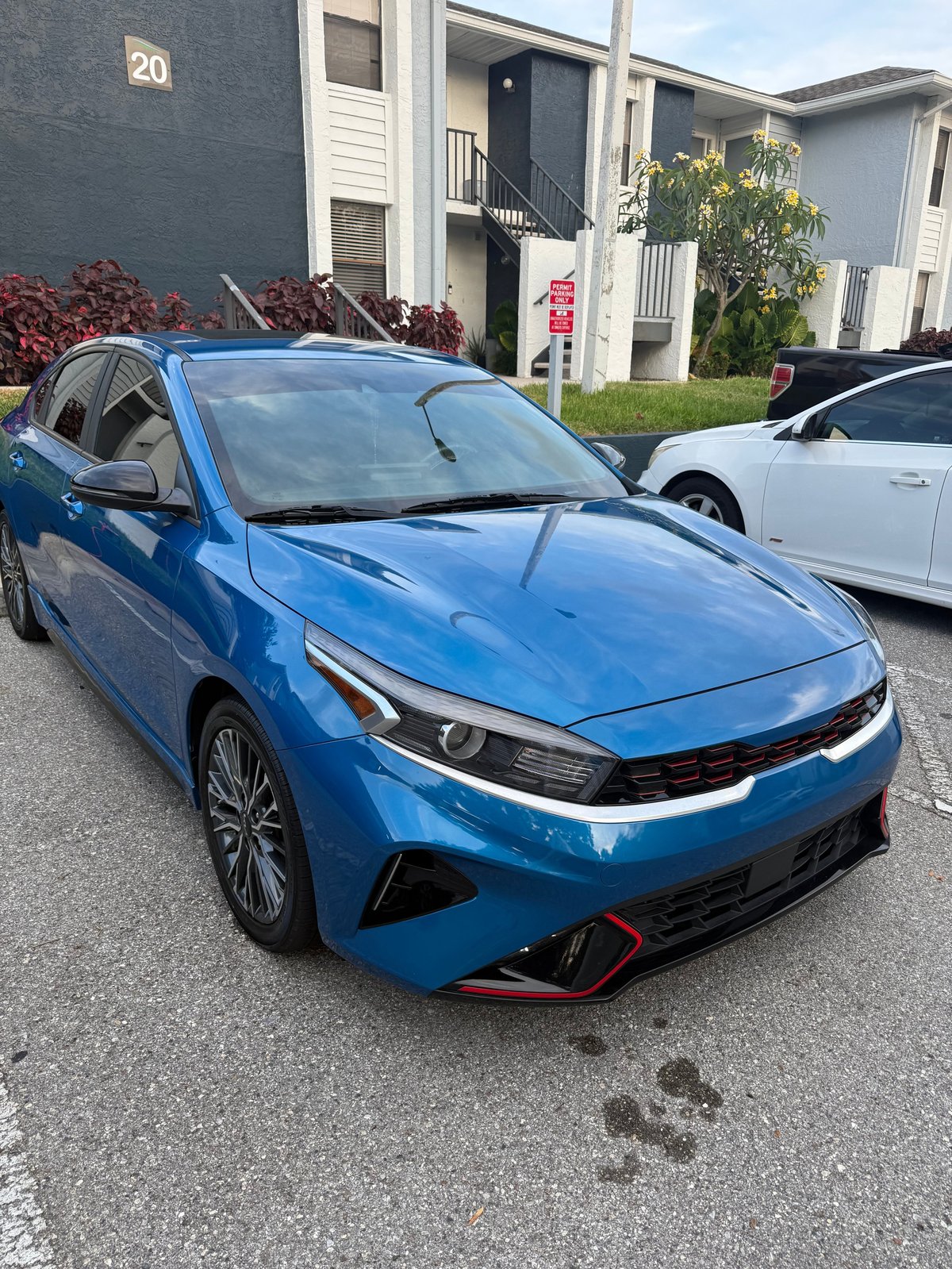 Bright blue Kia sedan parked in an apartment complex lot with residential buildings and another vehicle in the background