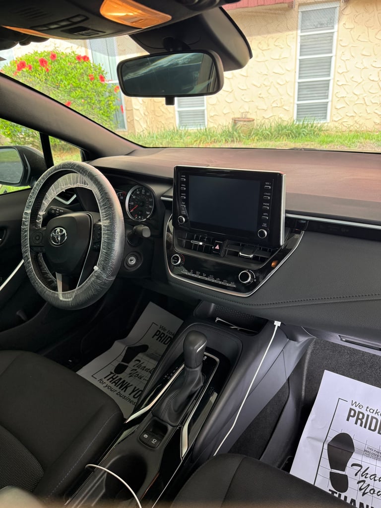 Interior view of Toyota vehicle showing steering wheel, dashboard with touchscreen display, and shift lever, parked in driveway